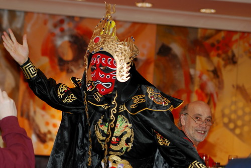 man dancing in traditional Chinese dress while wearing a mask.