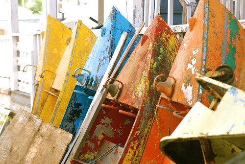 a series of brightly painted but rusting dinghies leaning against a wall.