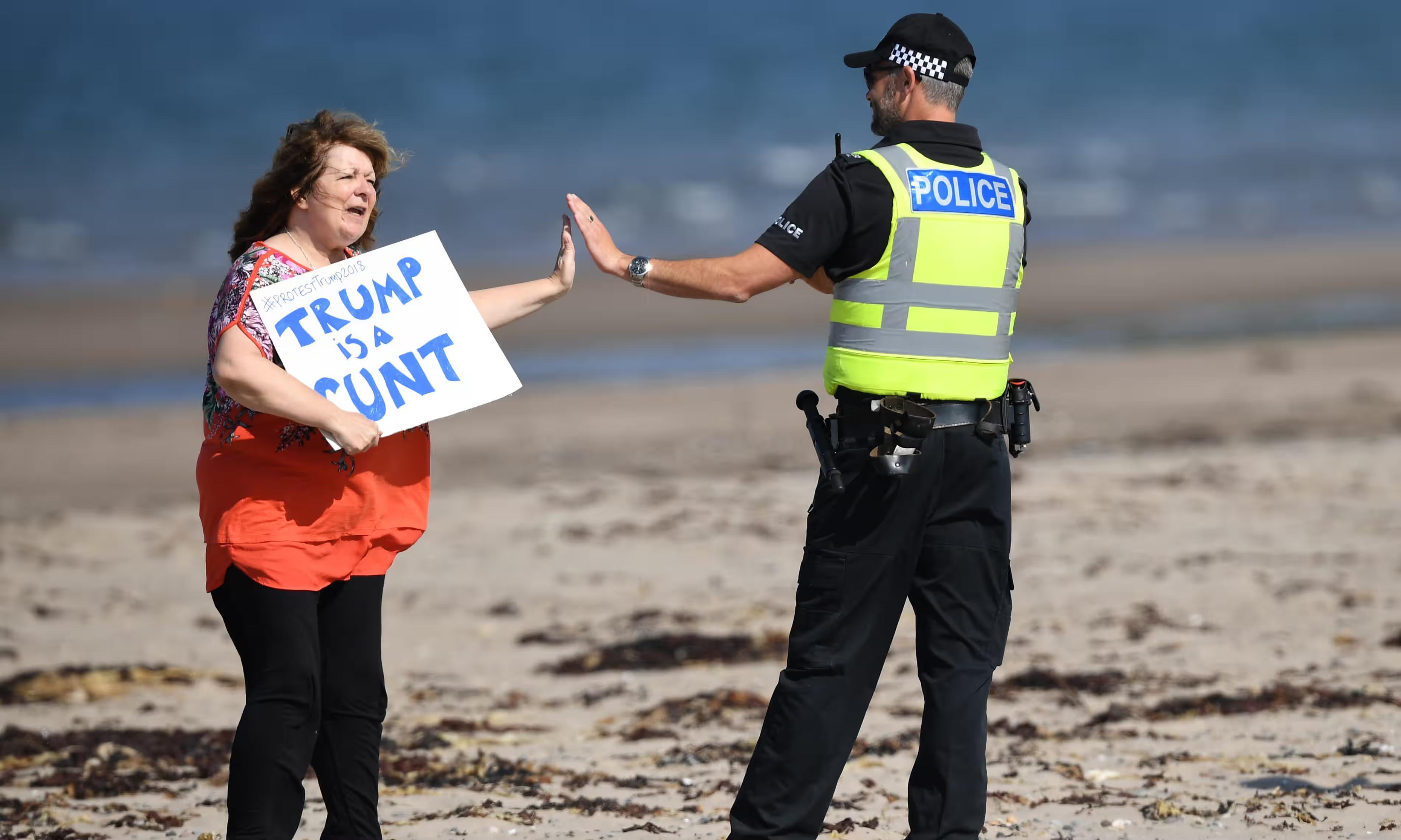 Scottish comedian and writer, Janey Godley high fives a policeman while carrying a Trump is A cunt sign