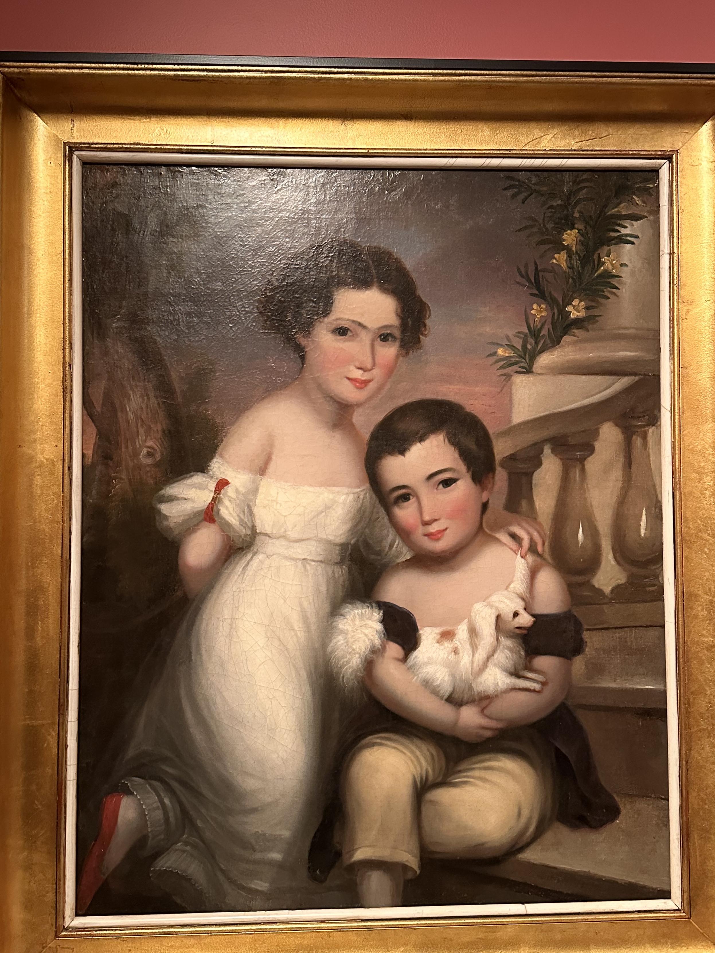 A painting of two children posing in a classic style - a boy and a girl. The girl is wearing a white dress and standing with her arm around the shoulder of the sitting boy. The boy is holding a very small white dog. The children’s features are painted too large for their faces and it makes the whole piece look cursed. 