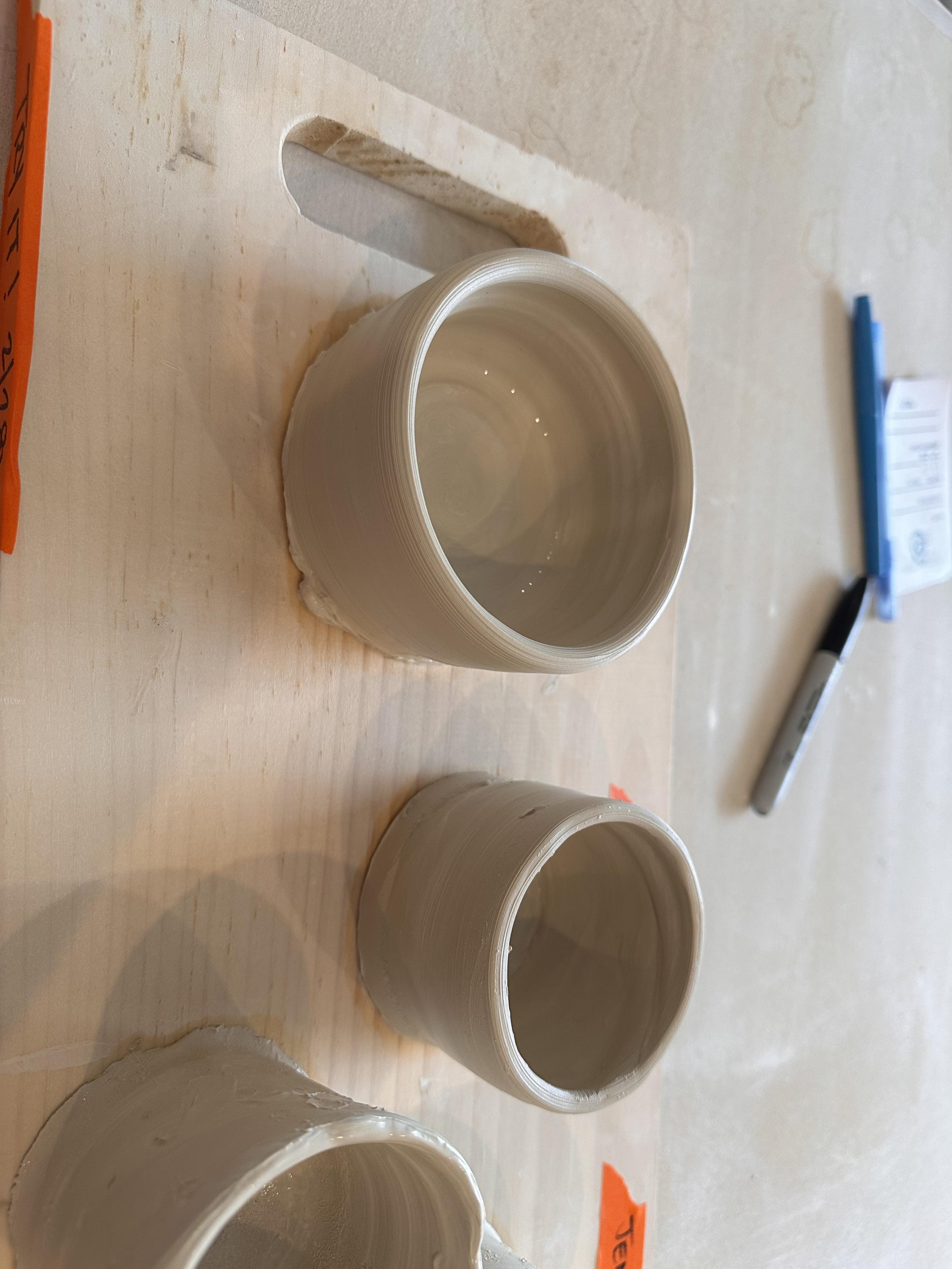 Two small unfired clay pots sitting on a board drying. 