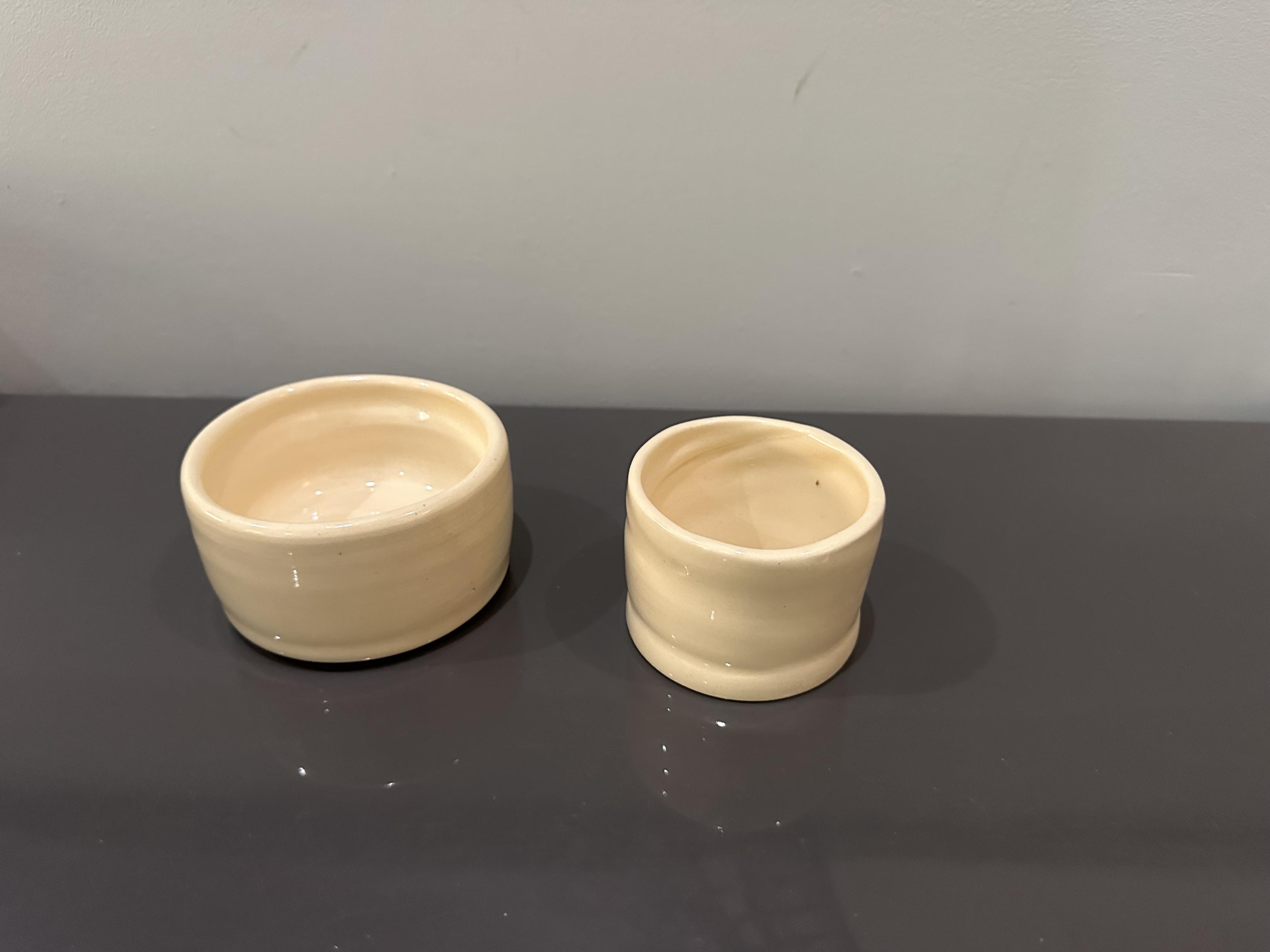 Two small ceramic pots. They have flat bottoms, mostly straight sides and clear glaze so they’re very light tan, the color of the fired clay. 
