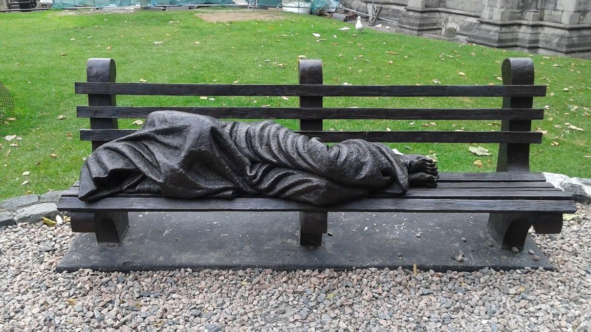 Jesus the Homeless statue outside a church in Dublin, Ireland. It's a bench with a man laying down covered by a blanket. His feet stick out, and you can see the piercings from the nails of the cross on them.