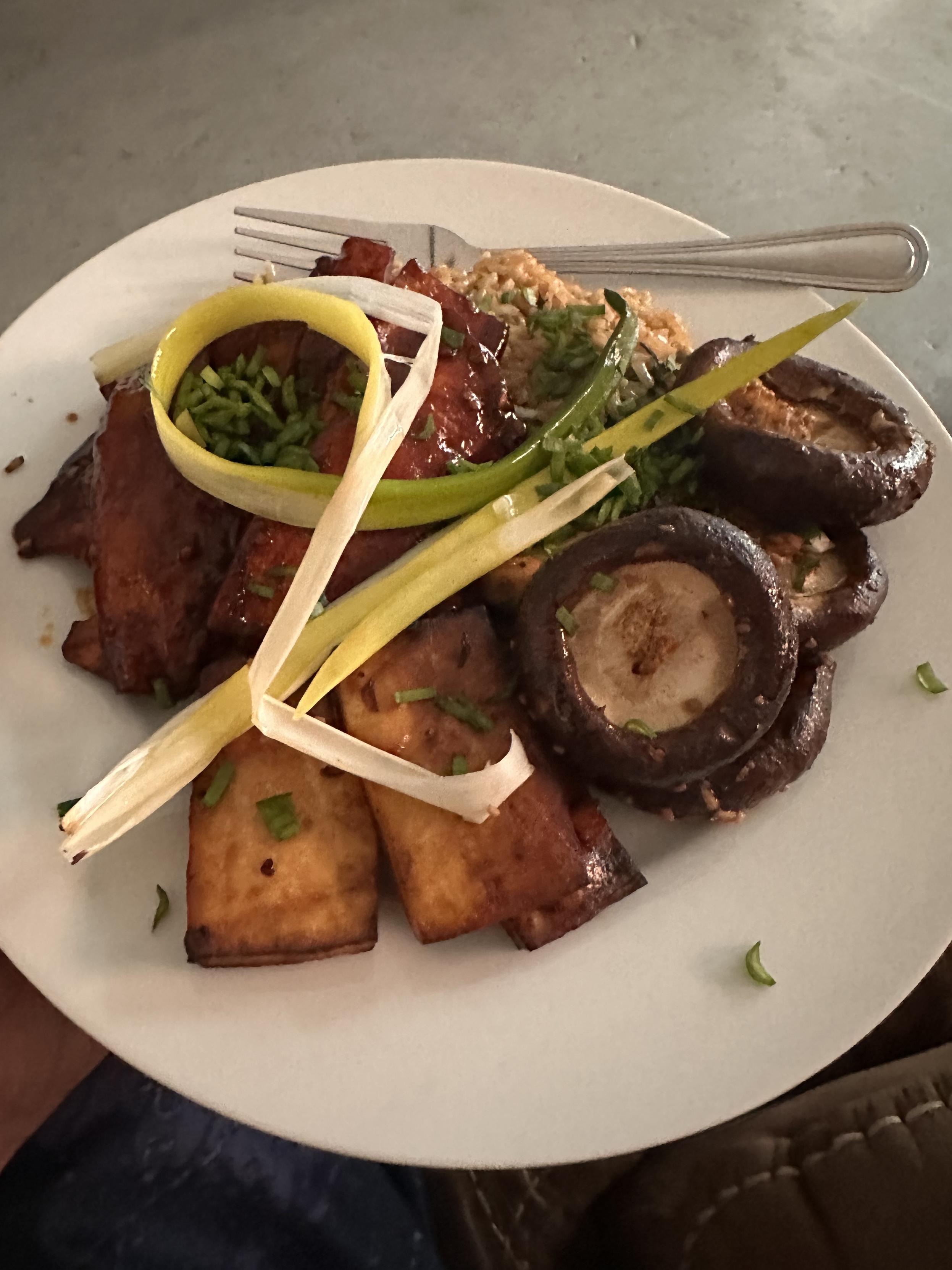 A plate of food: king oyster mushrooms marinated in Gochujang on top of rice next to baked shiitake mushrooms topped with a curly bit of green onion and sprinkled with chives. 