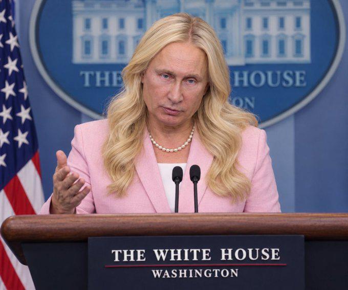 Putin appears as a woman with long blonde hair wearing pearls and a pink suit coat with a white blouse, standing at the White House press room lectern.